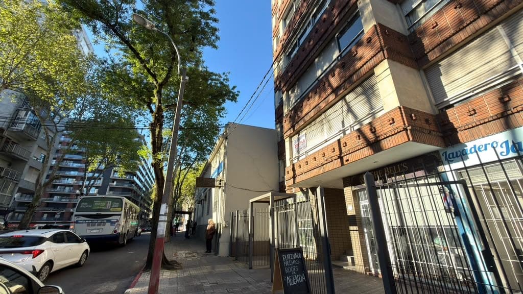 # Exterior - Urban Street Frontage
This image shows the exterior street view of a mixed-use urban building featuring a distinctive red brick facade on the upper levels with modern concrete and metal cladding on the lower sections. The property is located on an active city street with ground-floor commercial space (visible storefront with signage), residential units above, and is surrounded by mature street trees and neighboring mid-rise apartment buildings. The building appears to be in good condition with well-maintained architectural details and clear street-level access.
