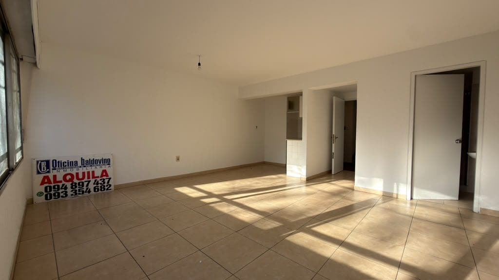 This is a spacious living room or open-plan living area featuring light beige ceramic tile flooring and neutral painted walls in excellent condition. The room is bright and airy with abundant natural light streaming through a large window on the left, and includes multiple doorways providing access to adjacent rooms or bedrooms. The space is unfurnished and move-in ready, with clean finishes and a modern, minimalist aesthetic.
WATERMARK: Oficina Baldovino